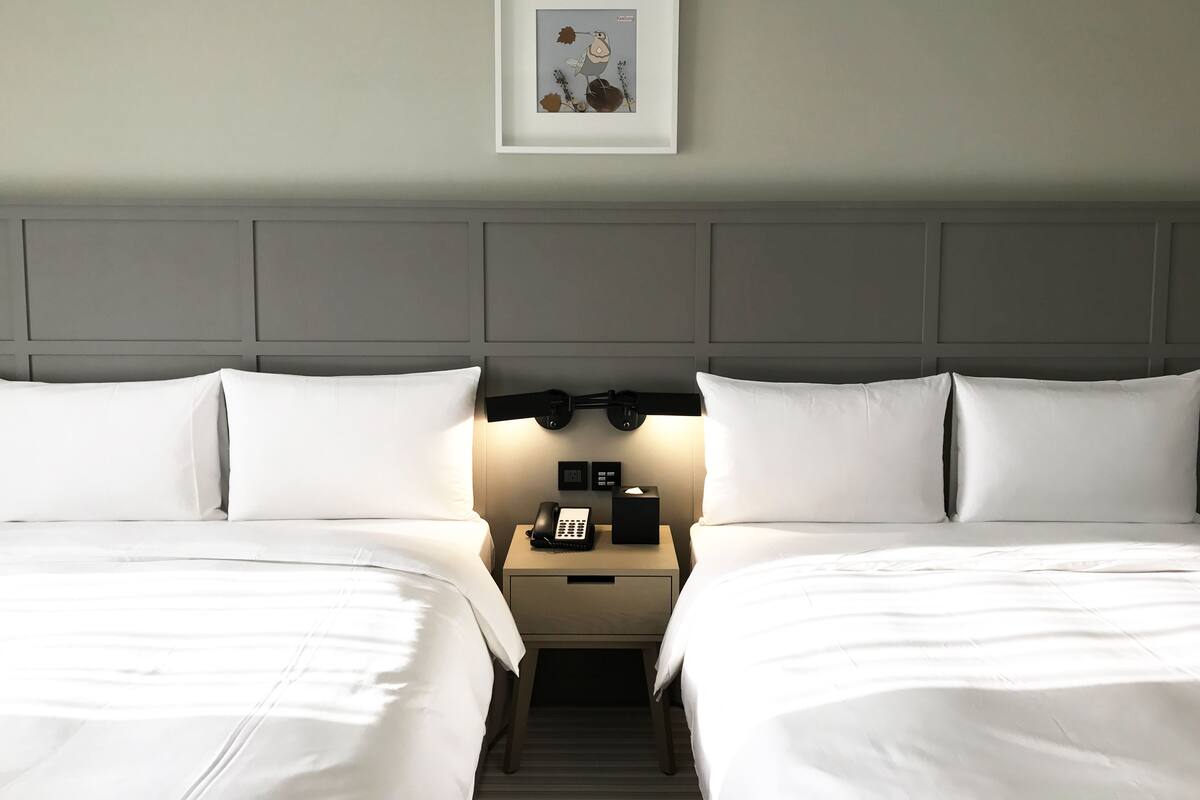 A hotel room with two beds, a nightstand with a phone, and a framed picture on the wall.