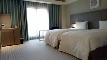 A hotel room with two beds, a desk, a chair, a clock on the wall, and a window with curtains.