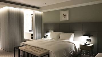 A modern hotel room with a large bed, a bedside table, a nightstand, a bench, and a window with blinds.