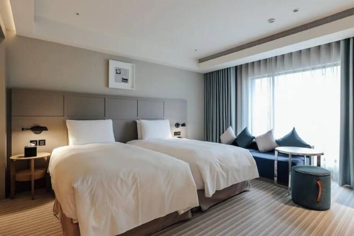 A hotel room with two beds, a sofa, a small table, and a trash bin.