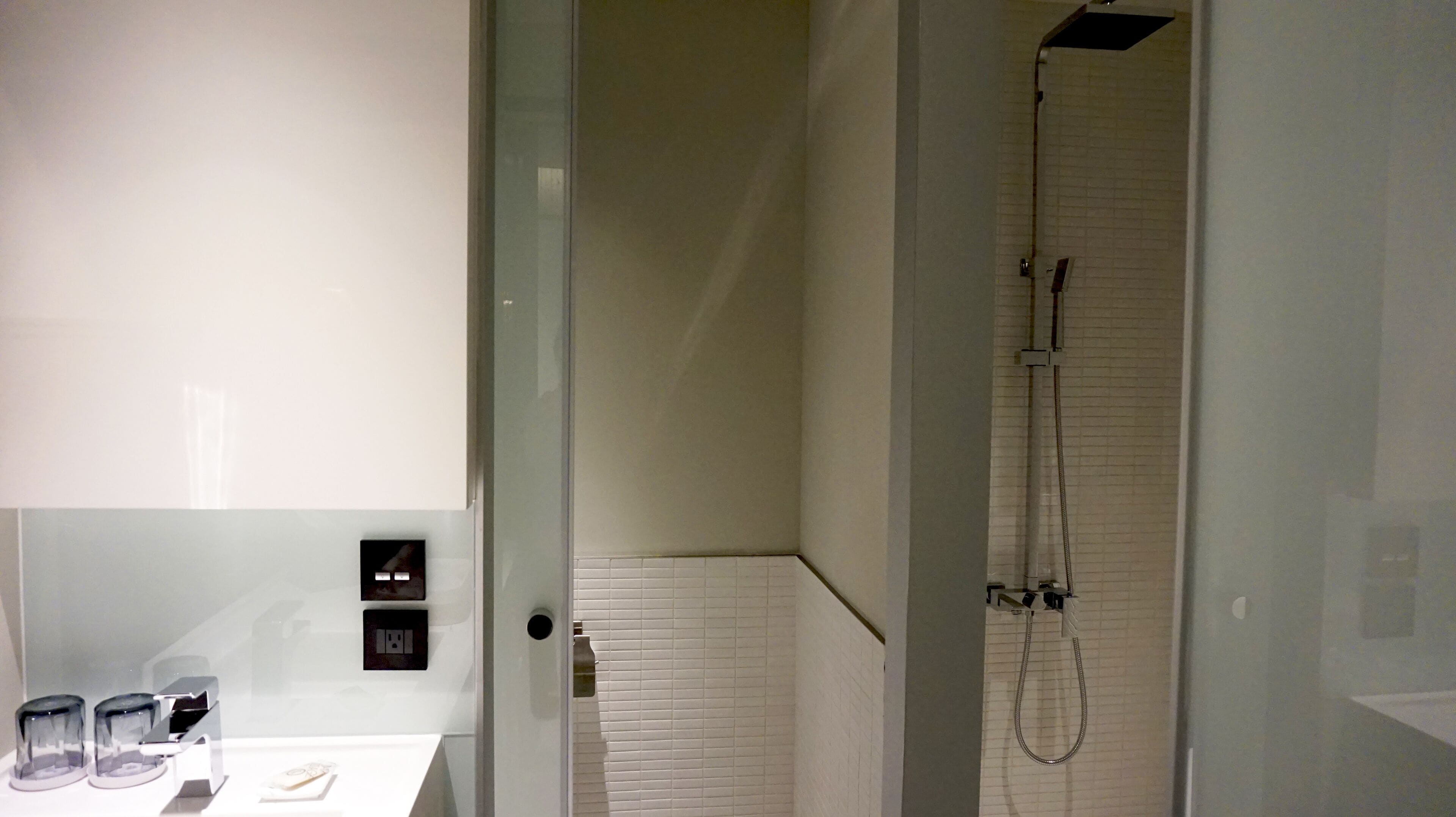 Un baño moderno con cabina de ducha de vidrio, paredes cubiertas de azulejos blancos y un diseño minimalista.