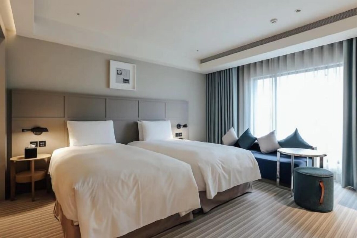 A hotel room with two beds, a sofa, a small table, and a trash bin.