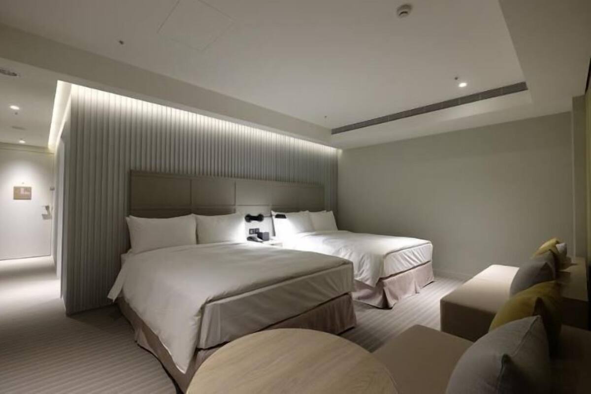 A modern hotel room with a large bed, a smaller bed, and a seating area with a round table.