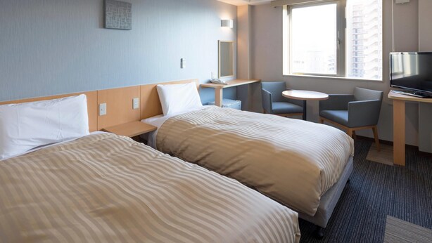 Een hotelkamer met twee bedden, een bureau met een televisie, een klein tafeltje en een stoel.