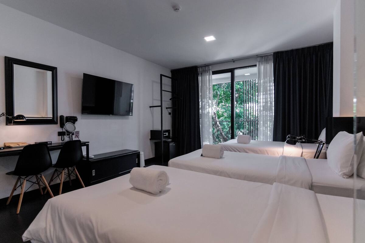 Une chambre d’hôtel avec deux lits, un bureau, une chaise, une télévision et une fenêtre avec des rideaux.