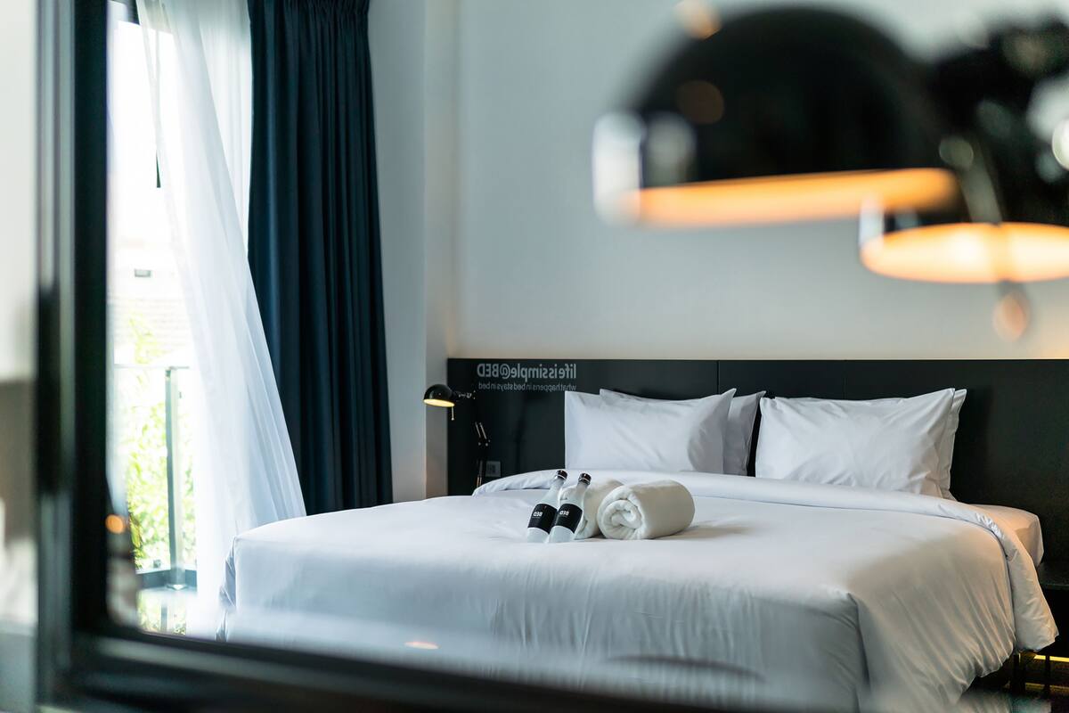Une chambre d’hôtel avec un lit bien fait, une tête de lit ornée d’une inscription et une fenêtre avec des rideaux.
