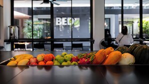 A fruit display on a table in a modern interior with large windows and a ceiling fan.
