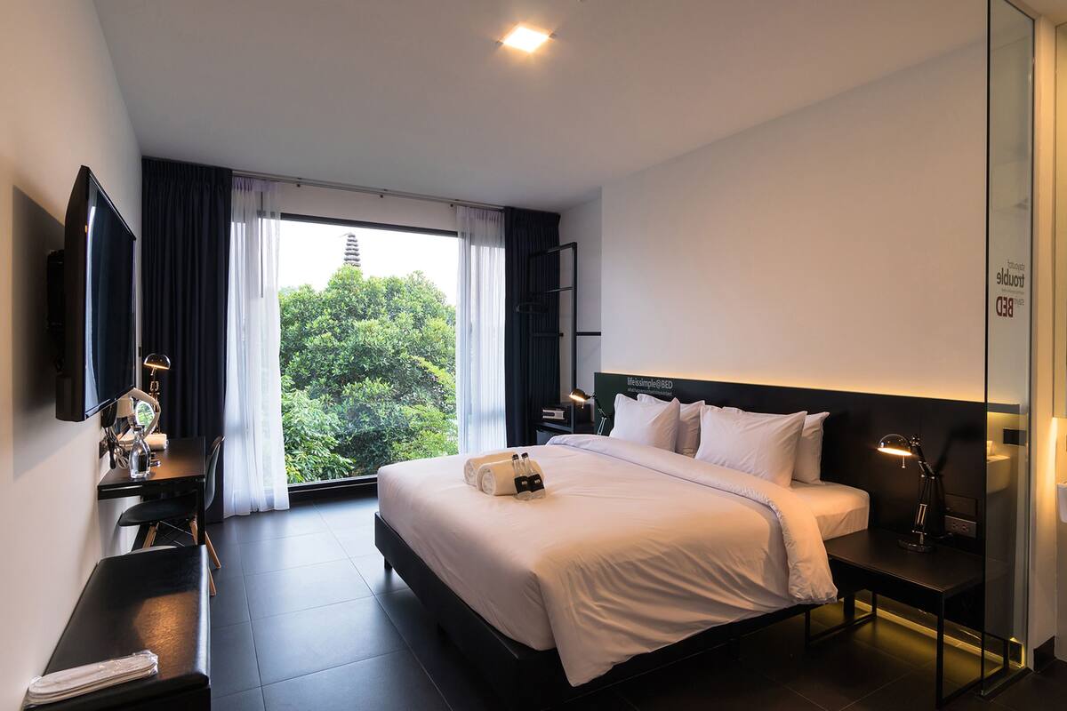 Une chambre d’hôtel moderne dotée d’un grand lit, d’un bureau, d’une télévision à écran plat et d’une fenêtre avec des rideaux.