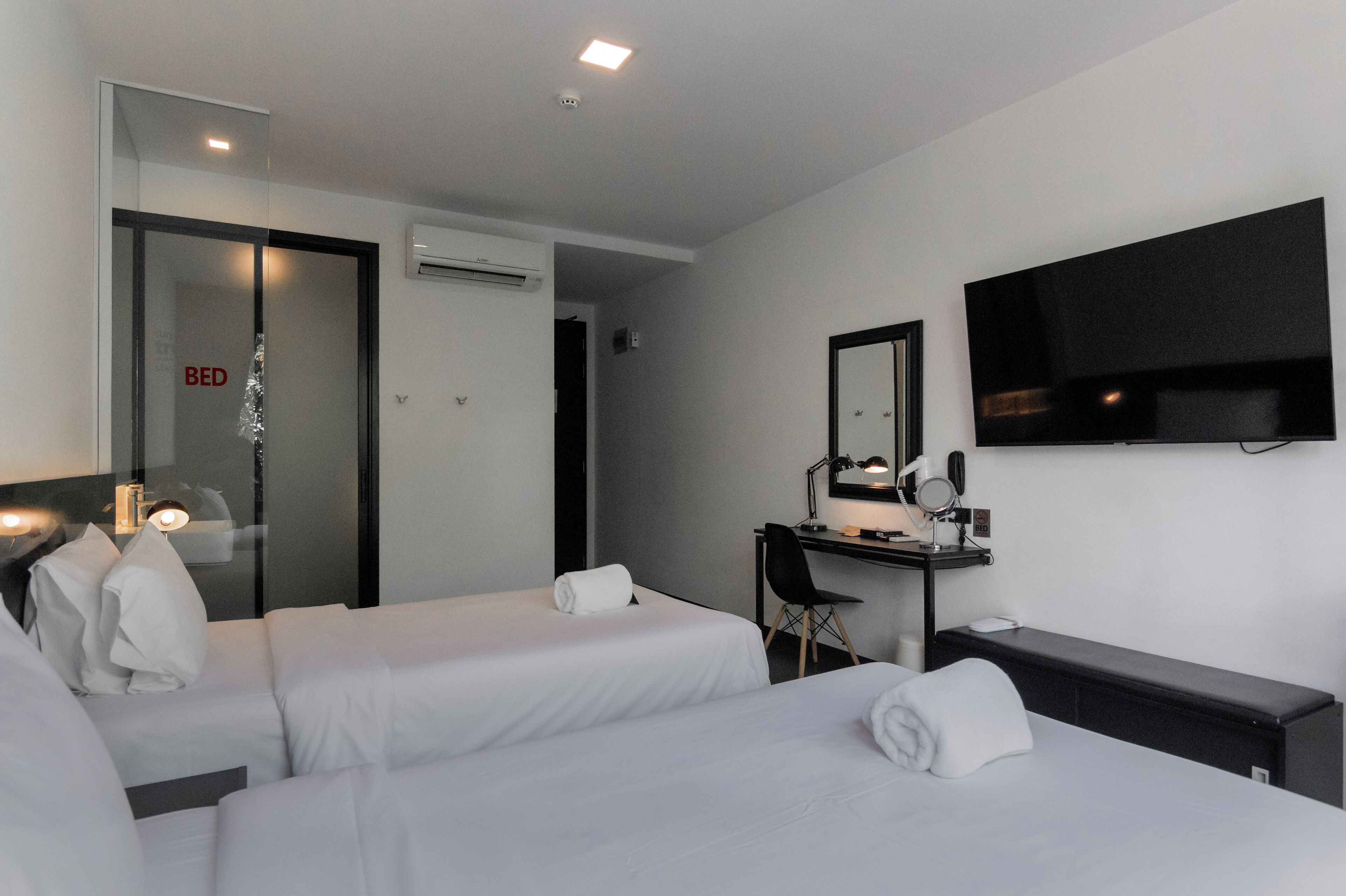 A hotel room with two beds, a desk with a chair, a TV, and a mirror.