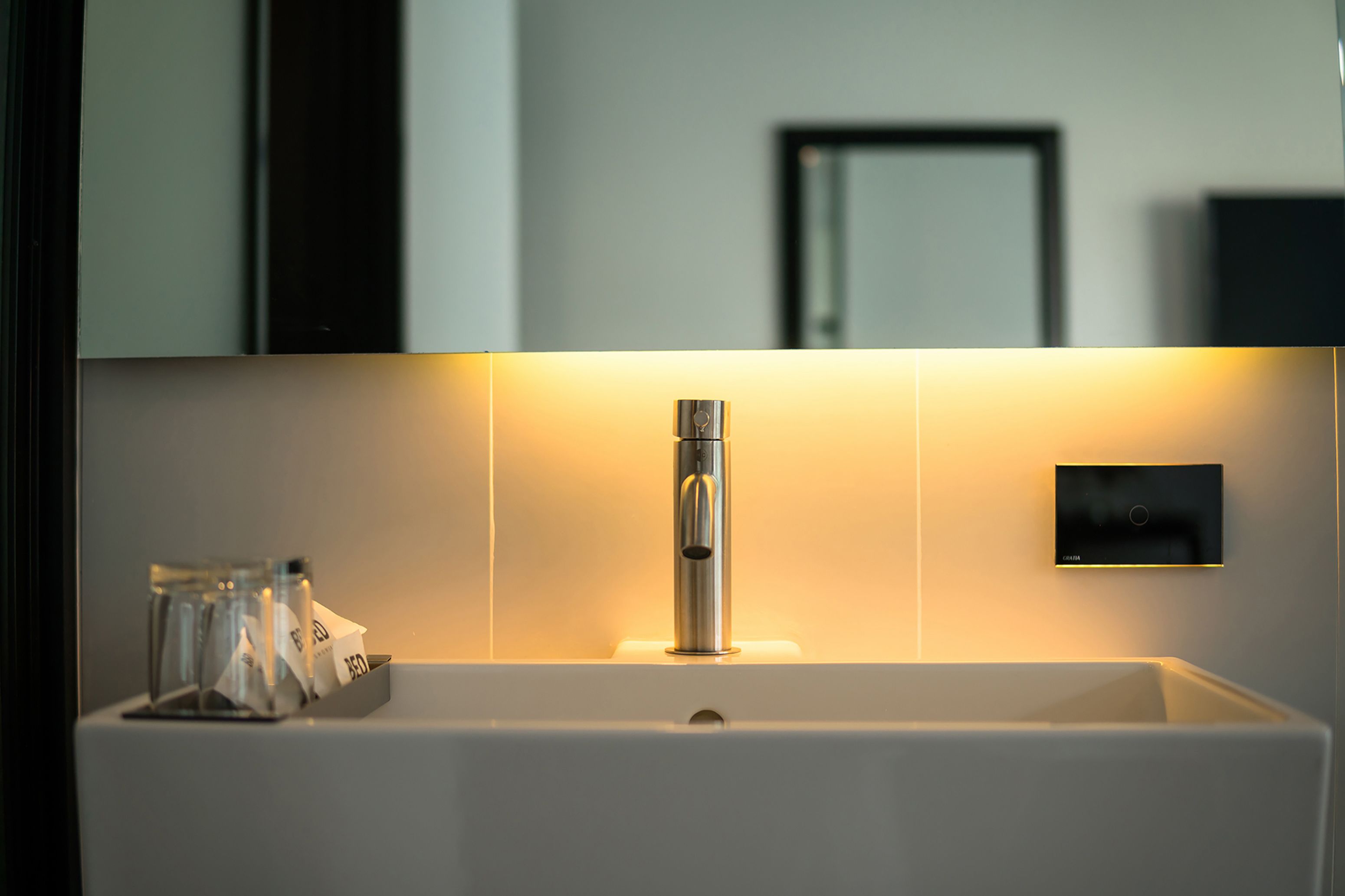 A modern bathroom with a white sink, a chrome faucet, and a wall-mounted control panel.