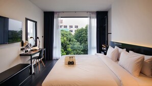 A hotel room with a large bed, a desk with a chair, a flat-screen TV, and a window with curtains.