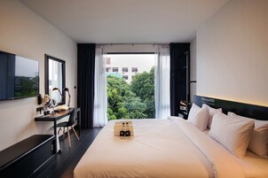 A hotel room with a large bed, a desk with a chair, a flat-screen TV, and a window with curtains.