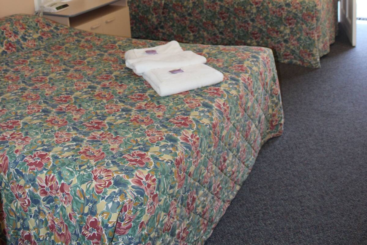 A hotel room with two beds, a mirror, a bedside table, and a window with curtains.