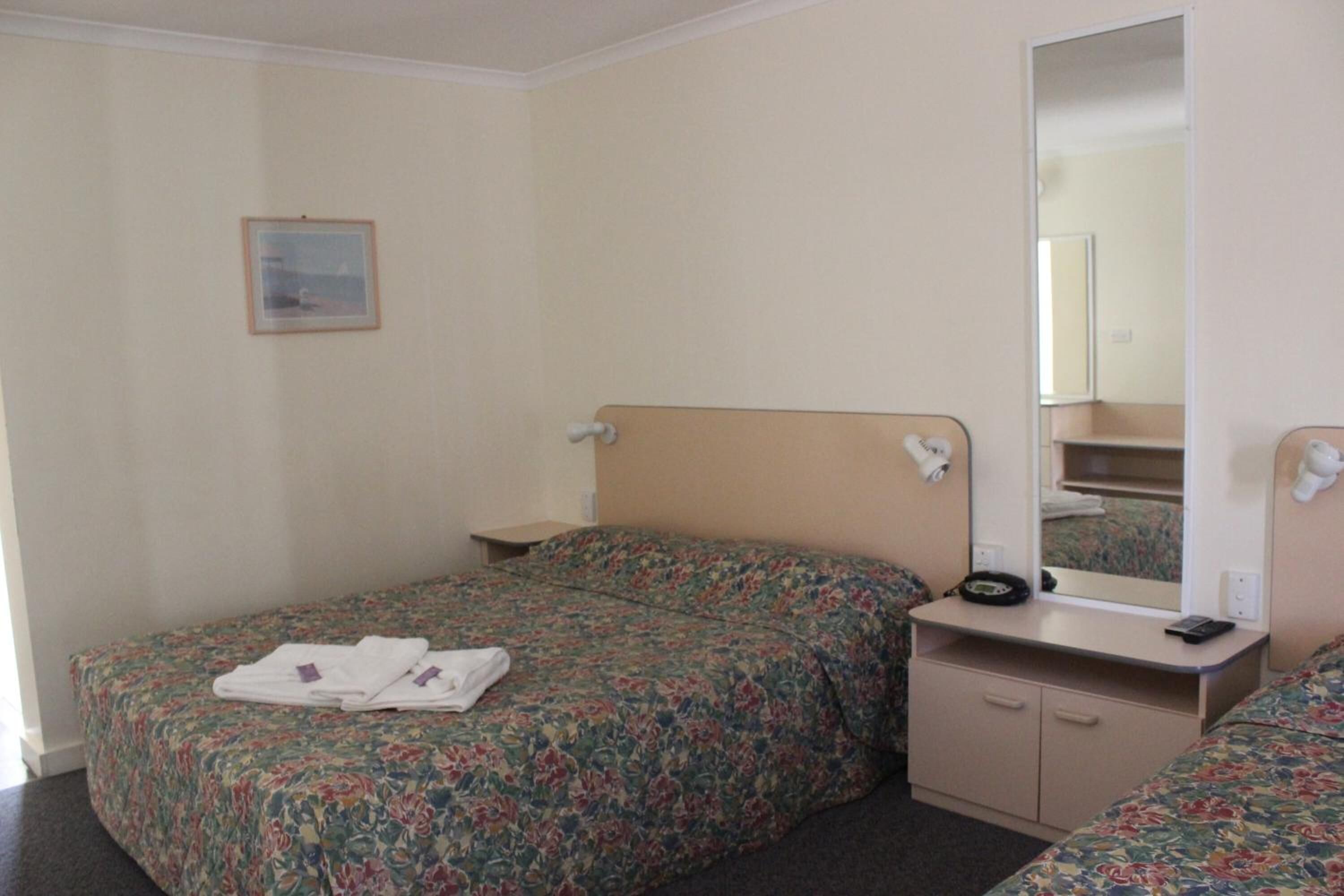 Habitación de hotel con dos camas individuales, una mesita de noche con lámpara, un espejo y un escritorio pequeño con teléfono.
