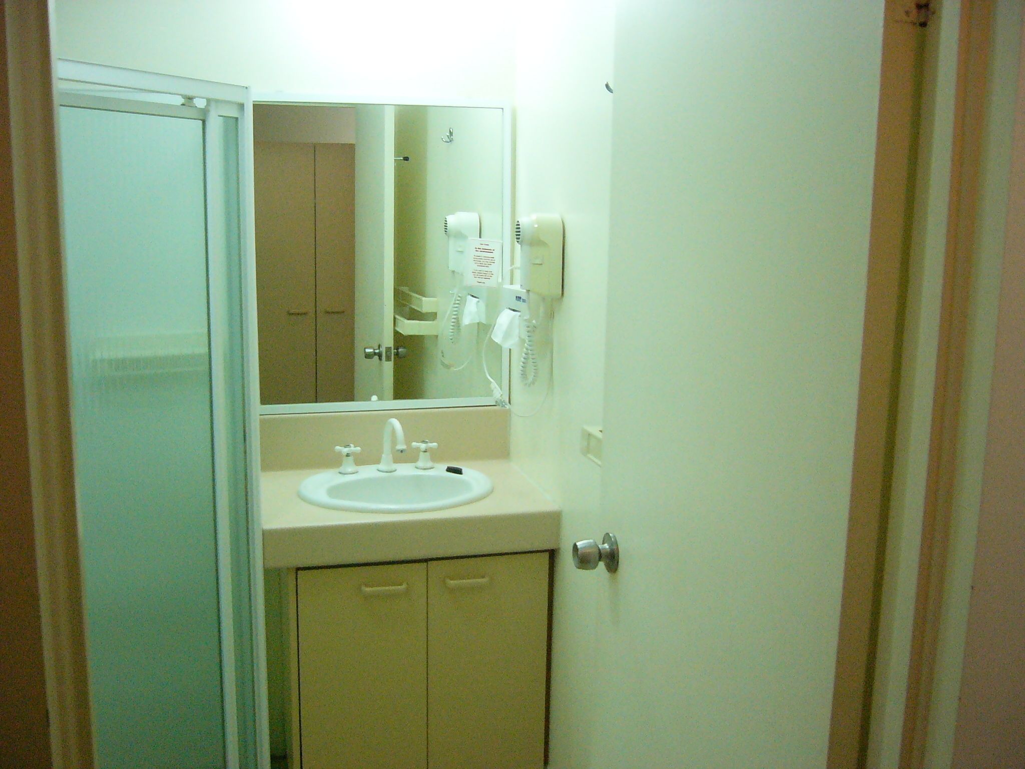 A small bathroom with a white sink, a mirror, and a hairdryer on the wall.