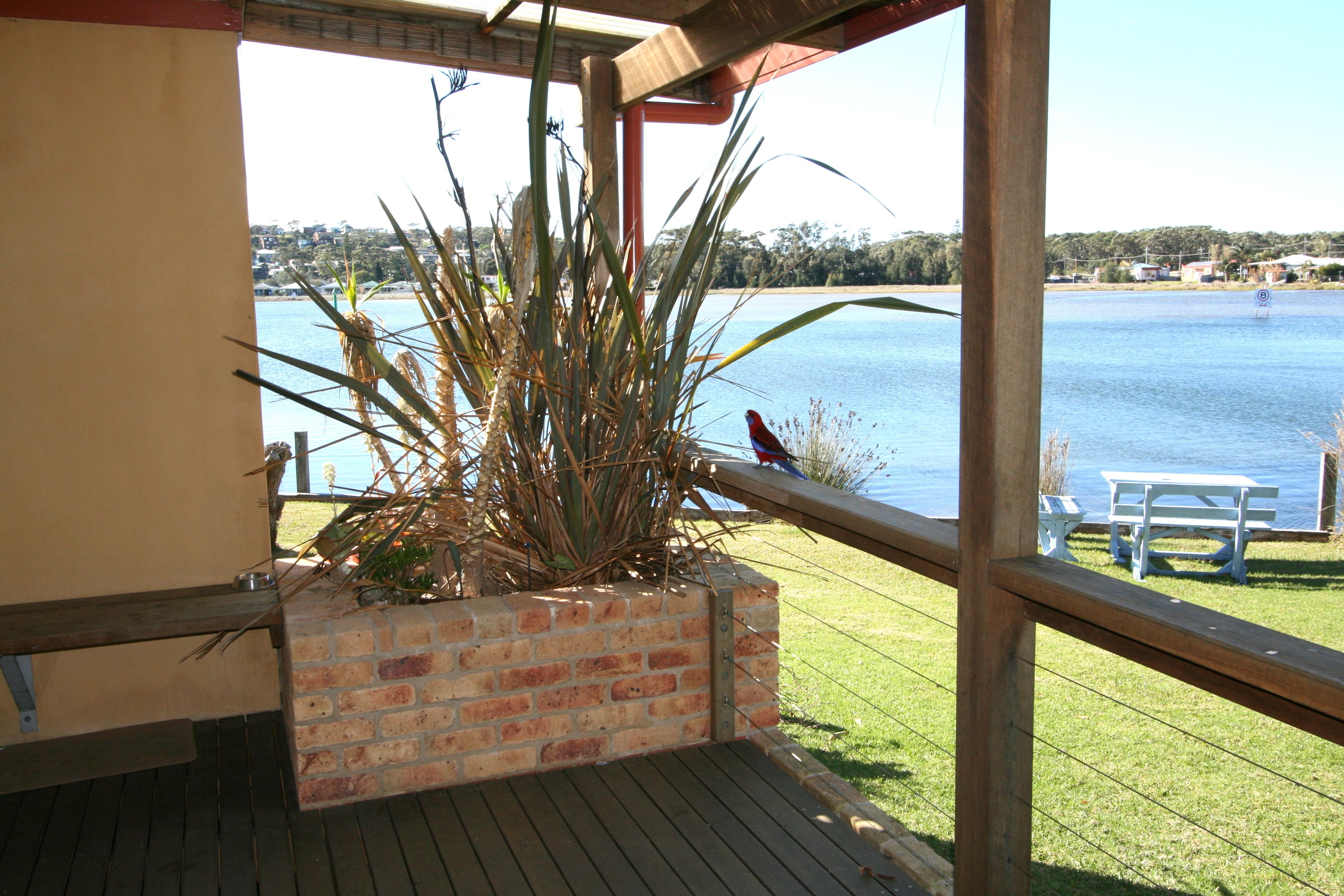 A balcony with a view of a lake, a wooden deck, and a brick planter with plants.