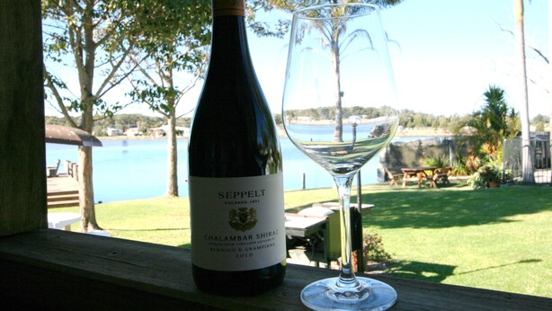 A bottle of Seppelt wine and a glass on a wooden ledge with a view of a lake and palm trees. - Lake Edge Holiday Units (Burrill Lake)
