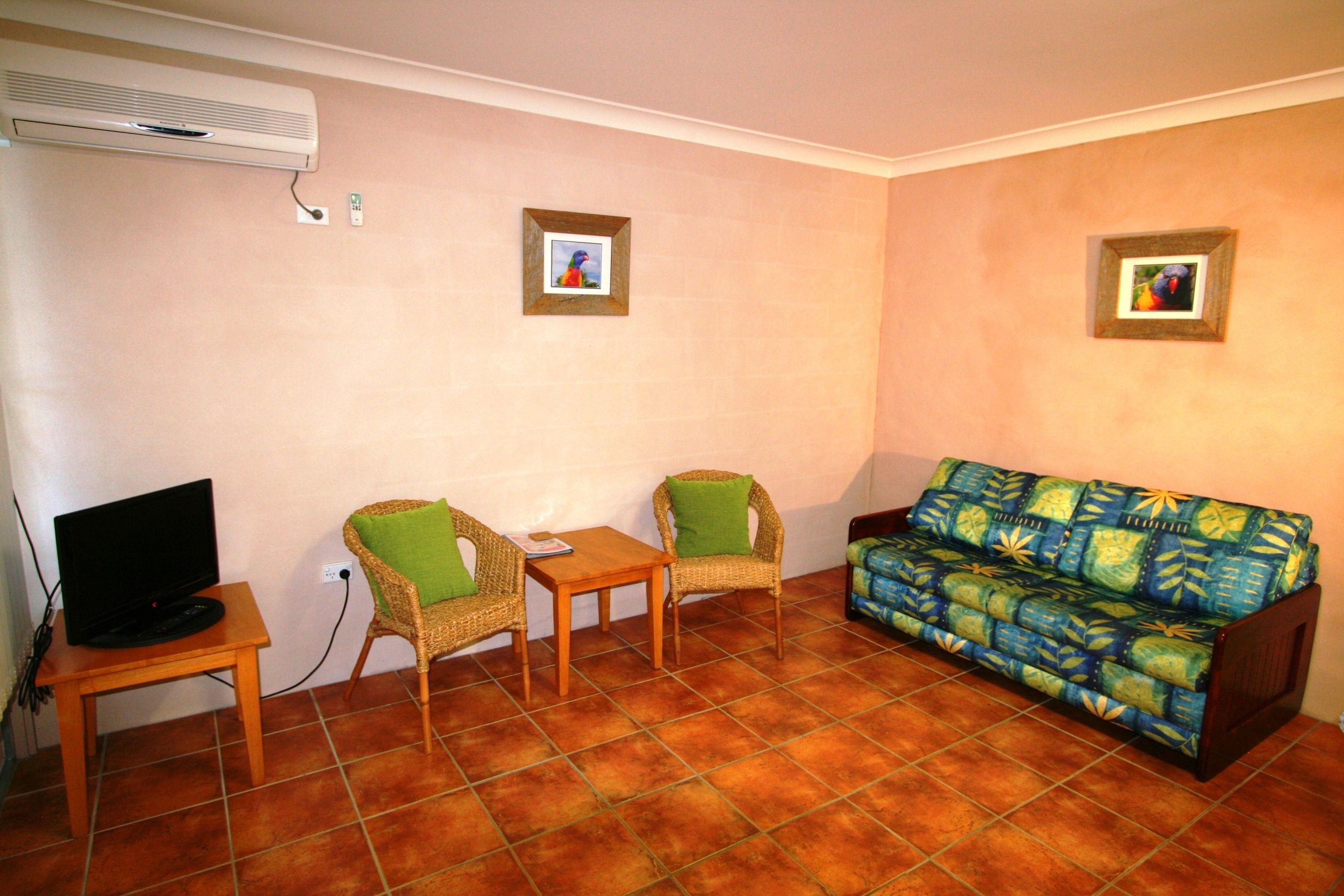 A living room with a television, two chairs, a small table, a sofa, and two framed pictures on the wall.