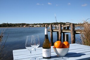 Una mesa con una botella de vino y un cuenco de naranjas junto a un lago con un muelle y casas al fondo.