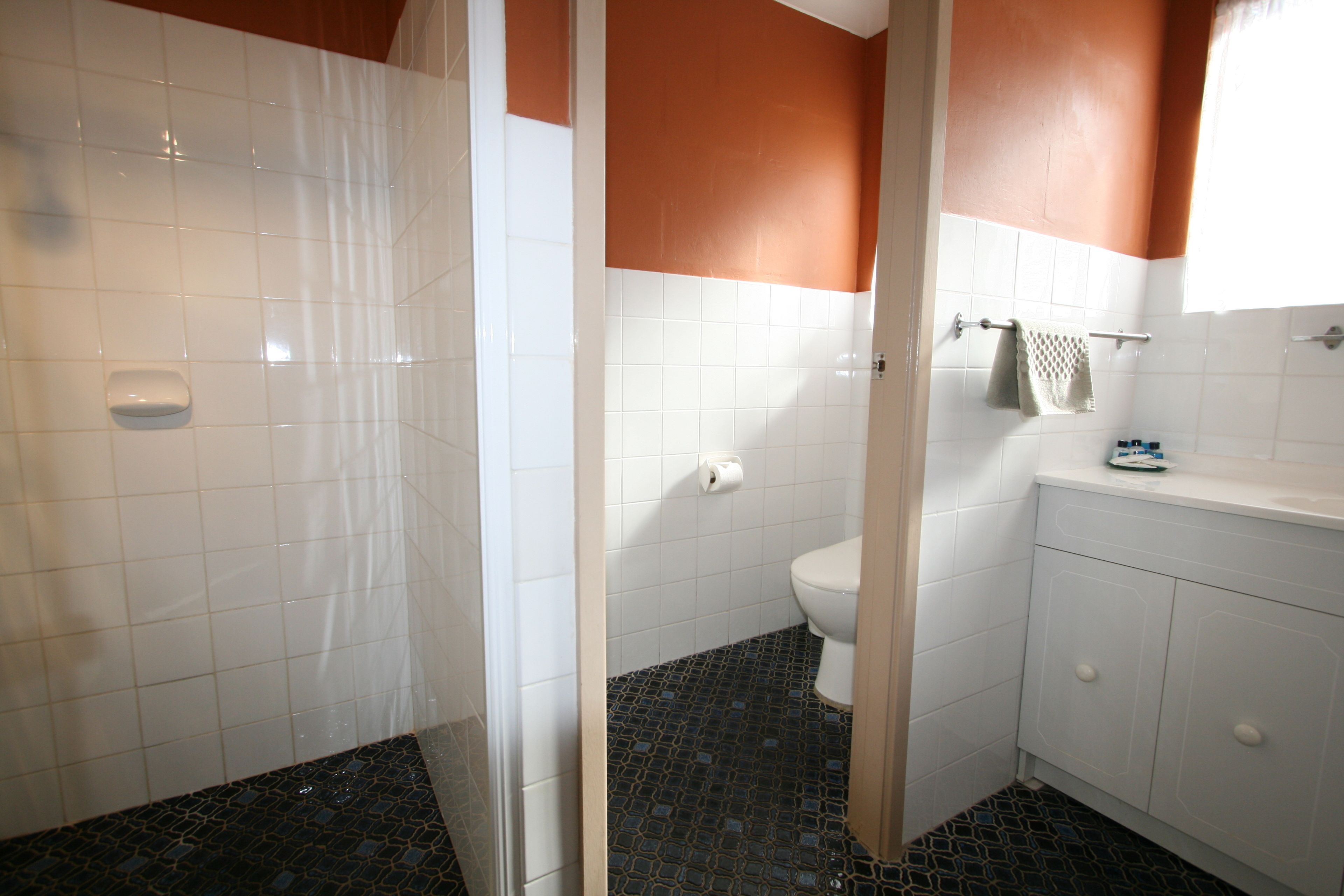 A bathroom with white tiles, a black and blue patterned floor, a white toilet, and a white sink with a towel rack.