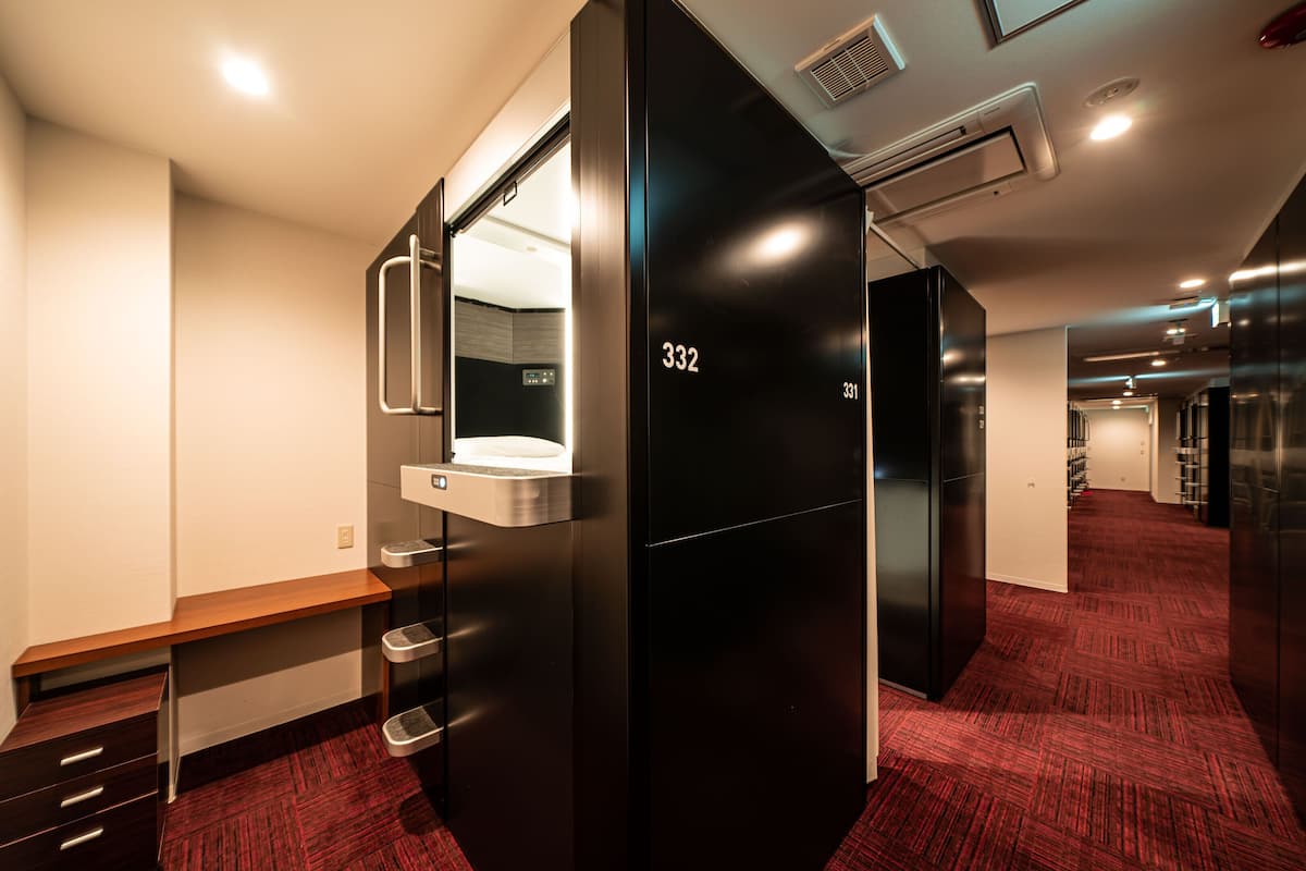 A modern hotel room with a black wardrobe, a bench, a mirror, and a red carpeted floor.
