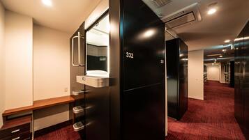Een moderne hotelkamer met een zwarte garderobe, een bankje, een spiegel en een vloer met rode vloerbedekking.