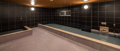 A modern indoor swimming pool with a wooden ceiling and black tiled walls.