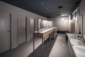A modern bathroom with multiple sinks, a vanity with mirrors, and a bench. - Capsule Plus Yokohama Sauna & Capsule (Yokohama)