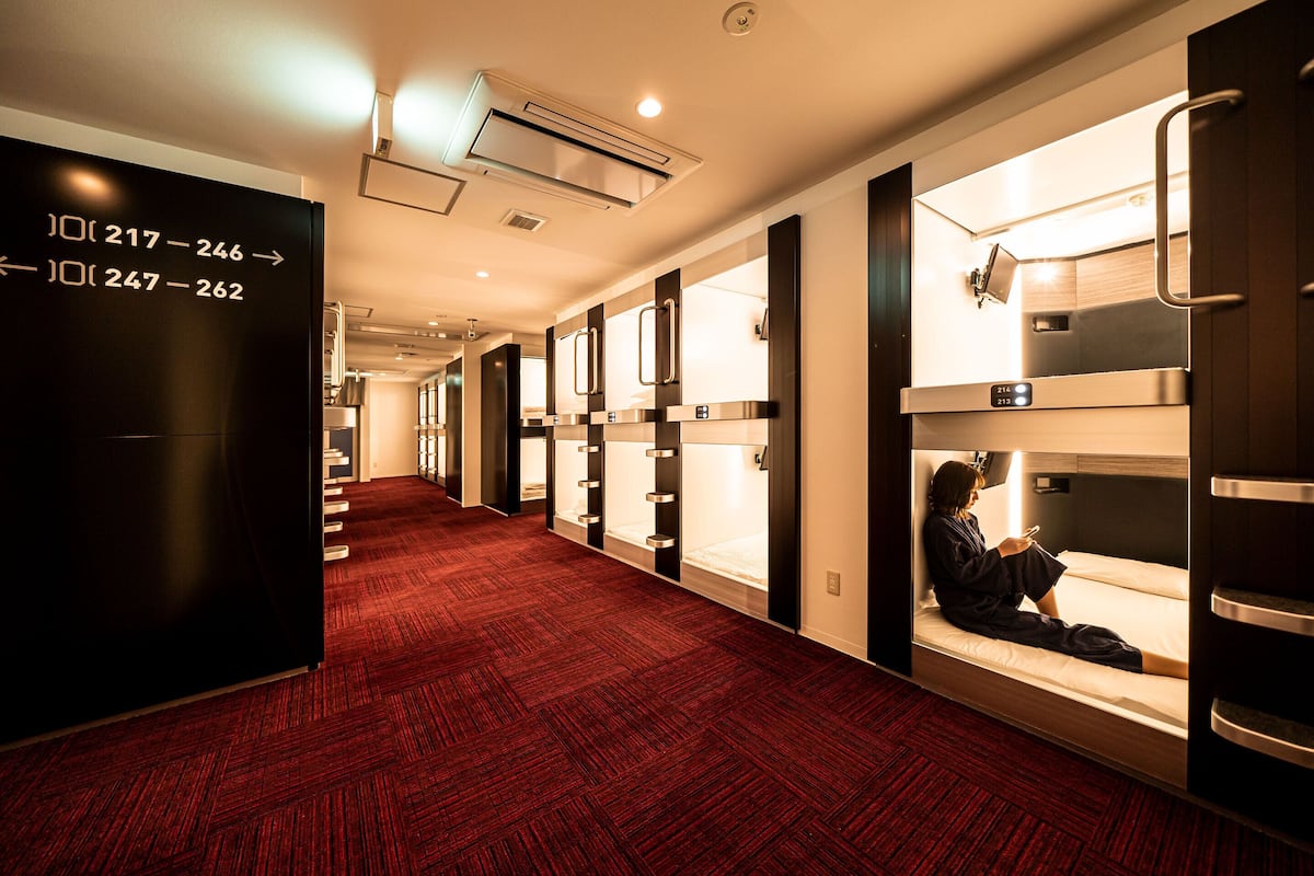 A hotel corridor with red carpet flooring, bunk beds, and a directional sign.