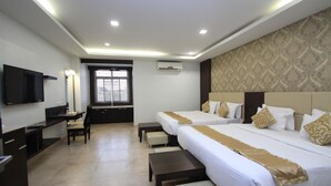 A hotel room with two beds, a desk, a chair, a TV, and a window.