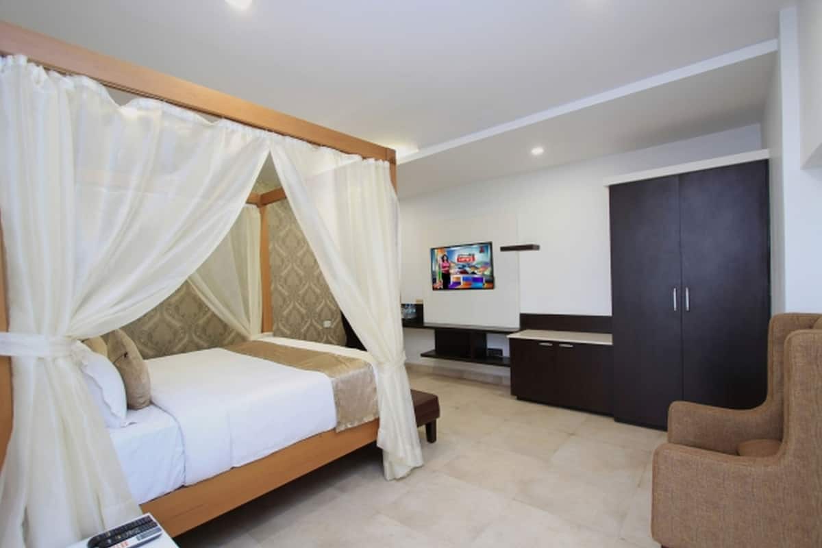 A bedroom with a canopy bed, a TV, a wardrobe, and a seating area.