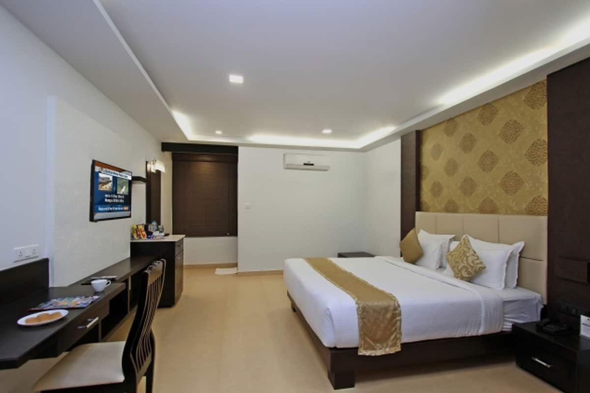 A hotel room with a bed, bedside table, desk, chair, and a poster on the wall.