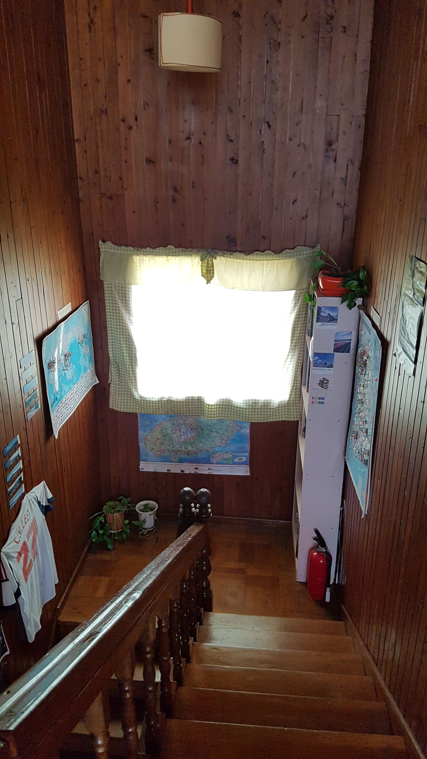 A wooden-paneled room with a window, a map on the wall, a refrigerator, and a fire extinguisher.