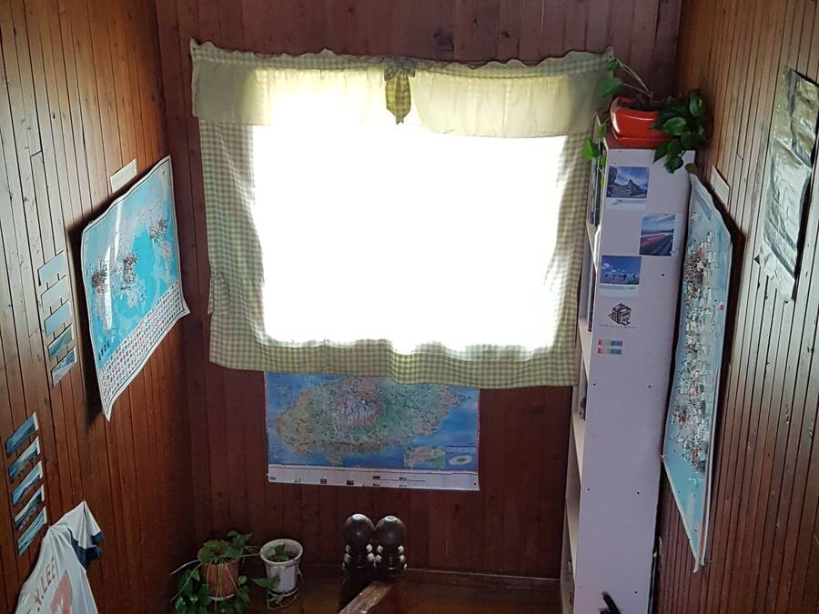 A wooden-paneled room with a window, a map on the wall, a refrigerator, and a fire extinguisher.