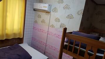A small room with a bed, a wooden headboard, a wall-mounted air conditioner, and a patterned wallpaper.