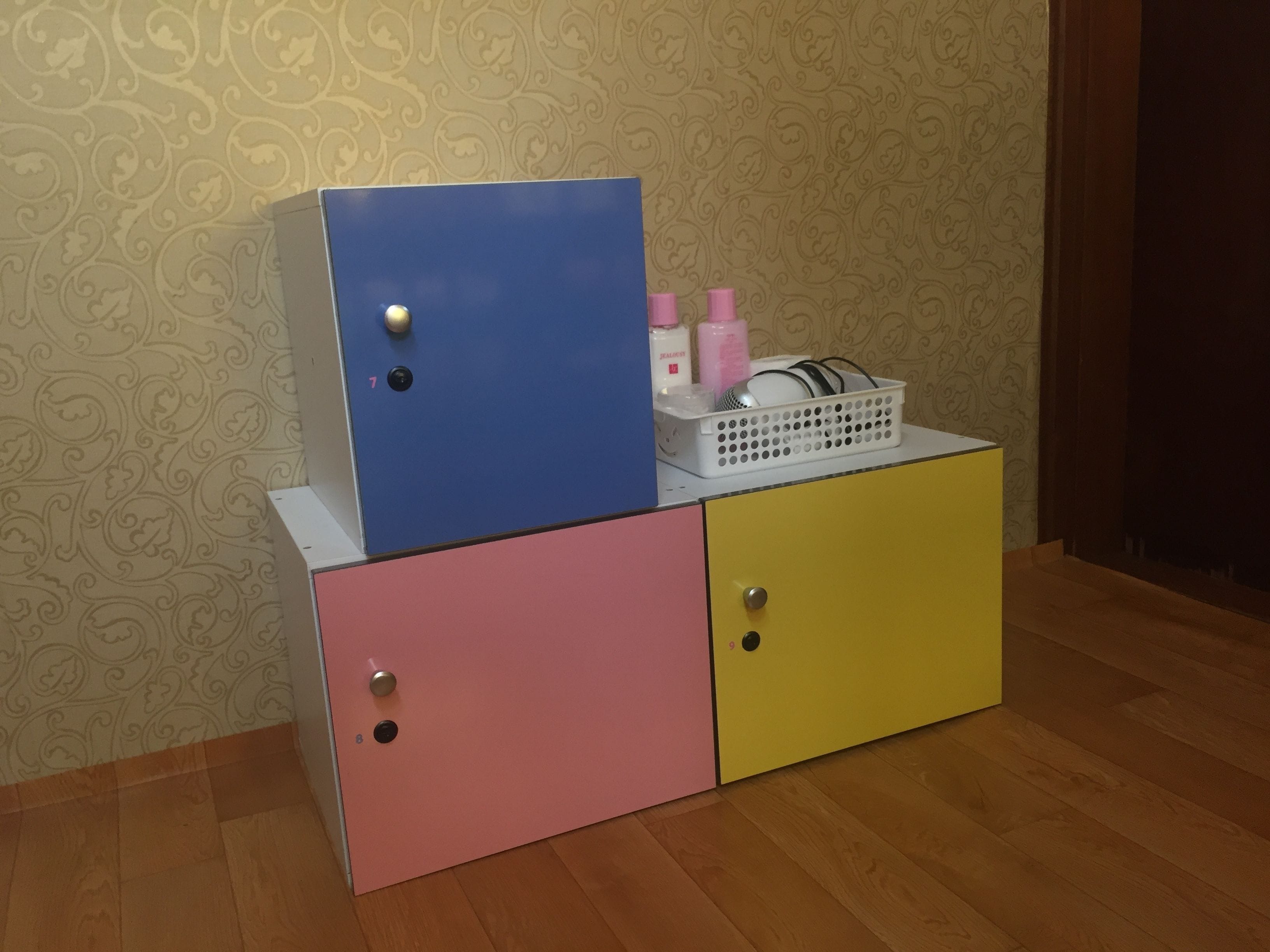 A multi-colored storage unit with drawers and a top cabinet, containing toiletries and a basket.