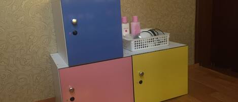 A multi-colored storage unit with drawers and a top cabinet, containing toiletries and a basket.