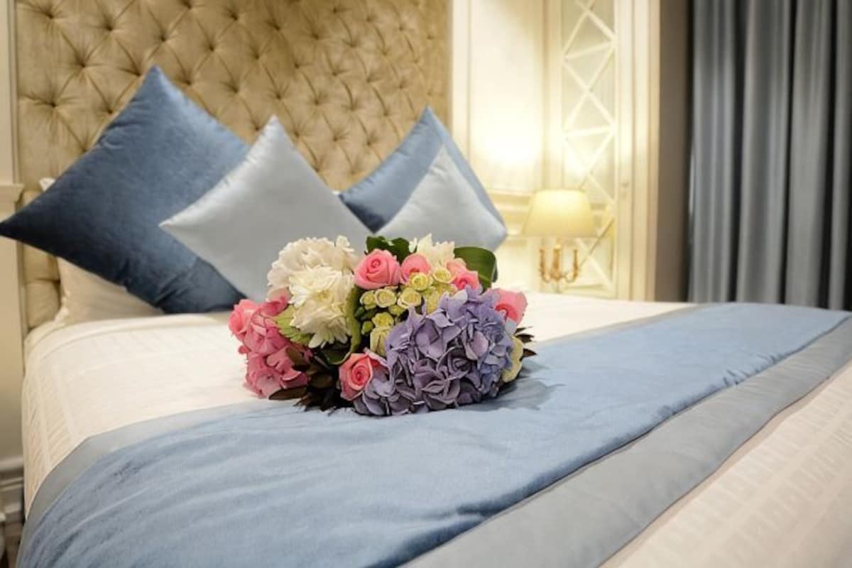 Uma cama com um edredom azul, um buquê de flores e dois travesseiros azuis.