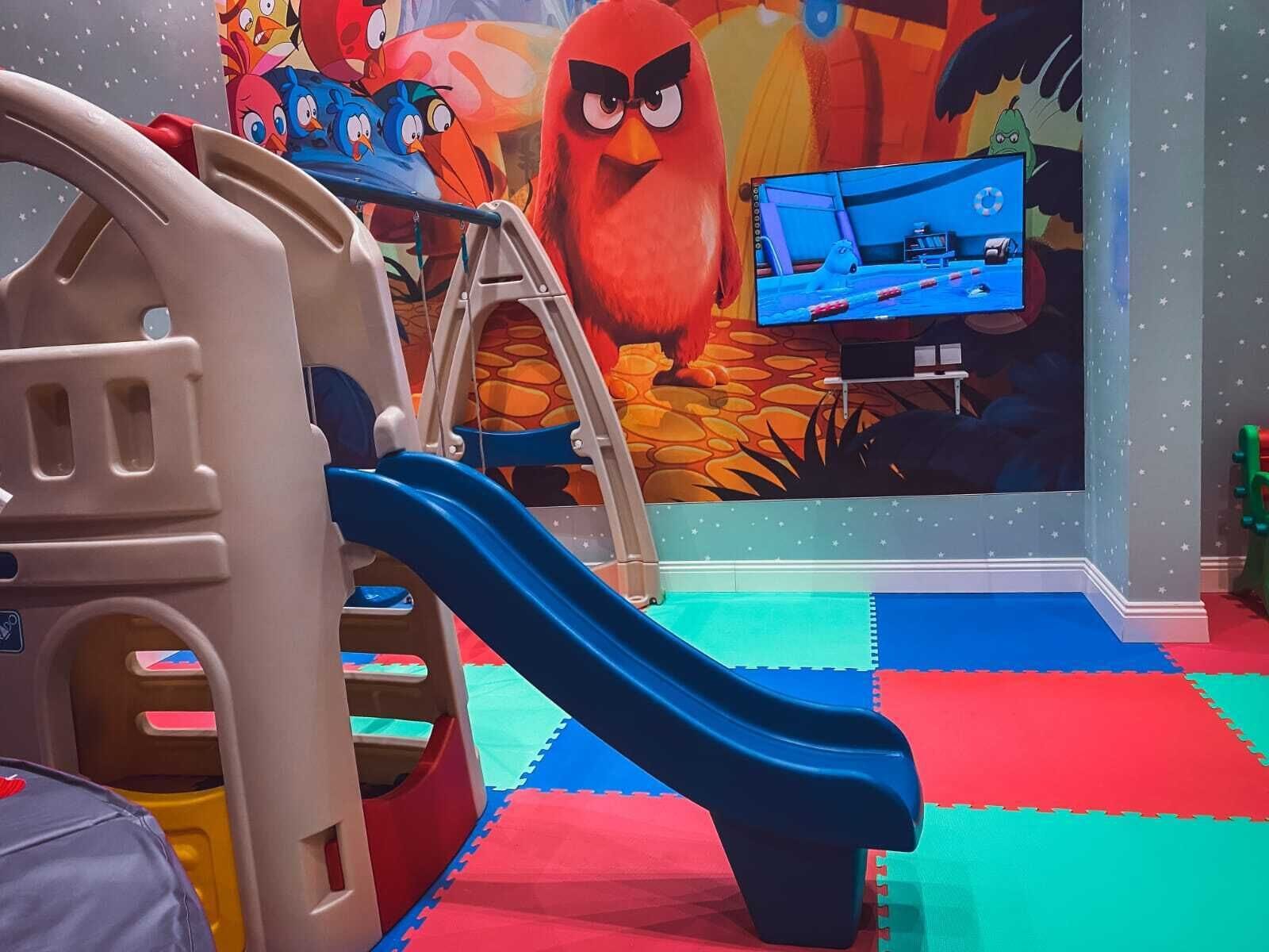 Zona de juegos infantiles con tobogán, estructura para escalar y un mural.