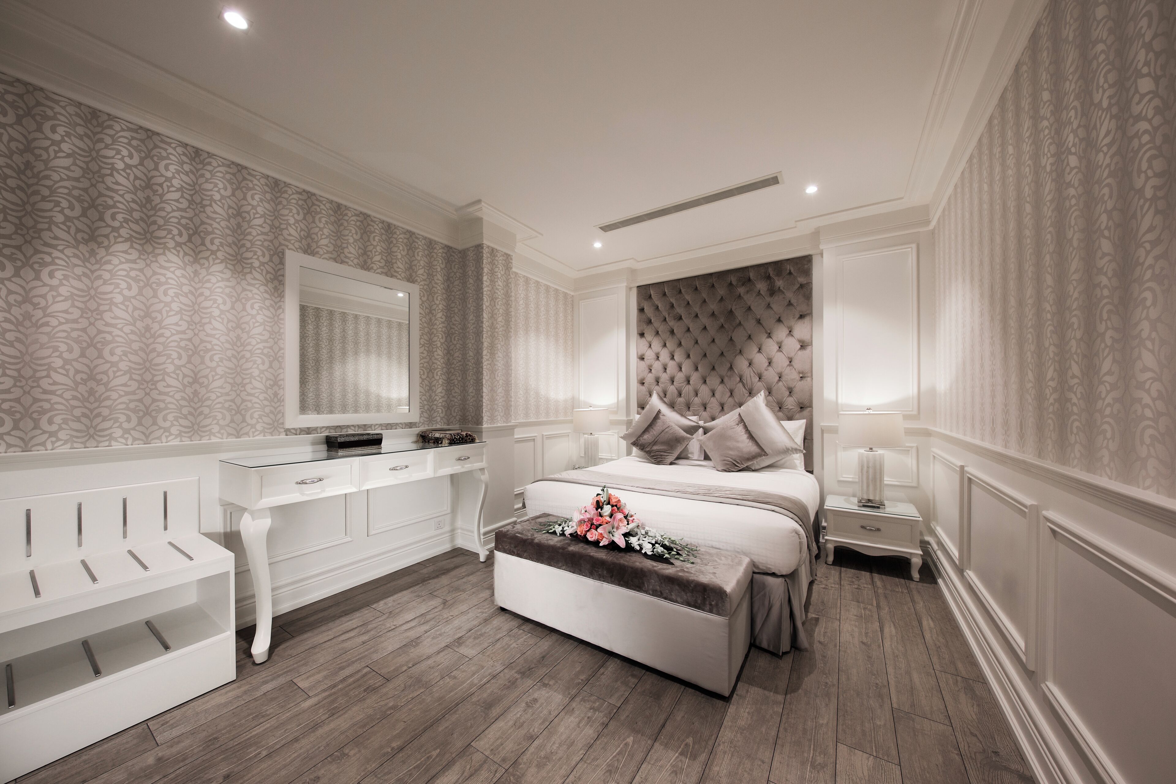 Un dormitorio con cama, tocador, banco y mesita de noche.