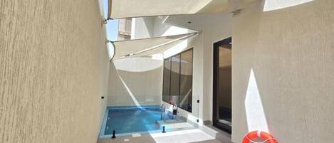 A pool area with a lifebuoy, a glass door, and a sunshade.
