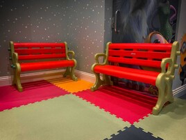 Dois bancos vermelhos com detalhes dourados em um quarto com paredes em padrão de estrelas e tapetes de chão coloridos entrelaçados.