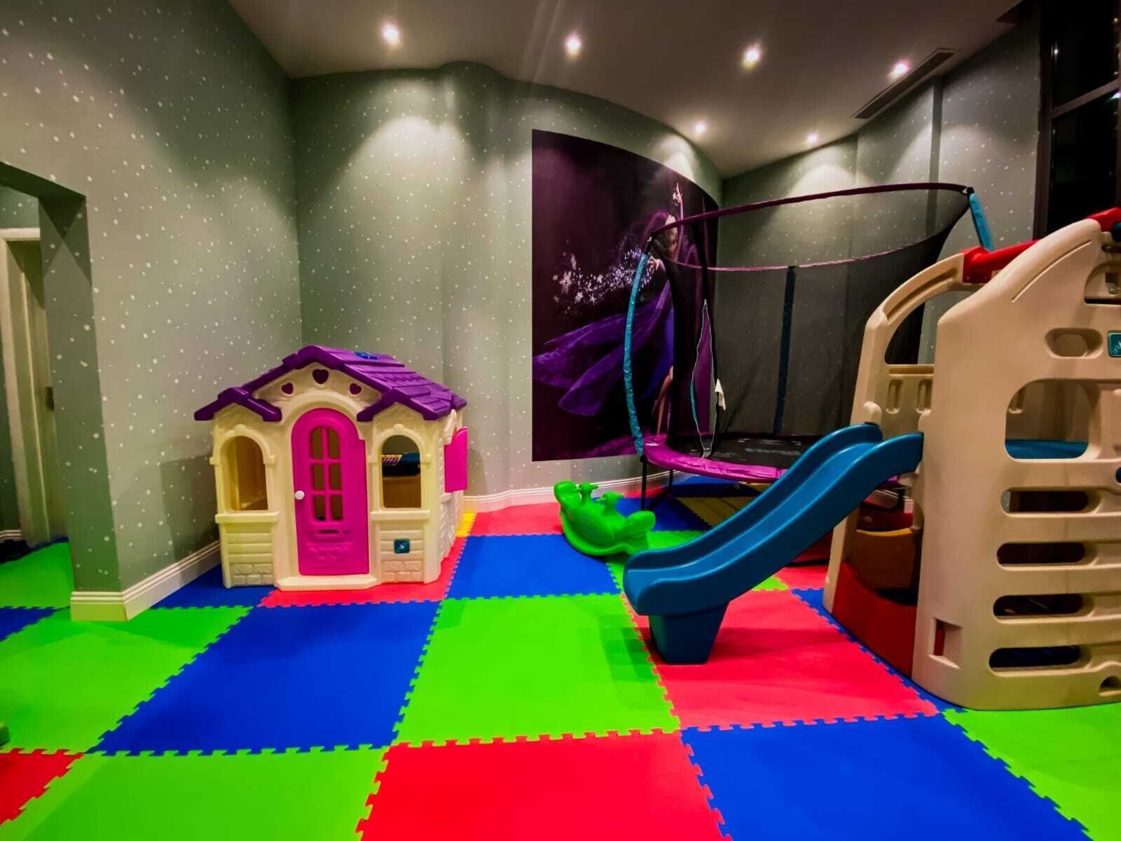 Een speelruimte met een poppenhuis, een trampoline en een glijbaan.