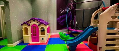 Een speelruimte met een poppenhuis, een trampoline en een glijbaan.