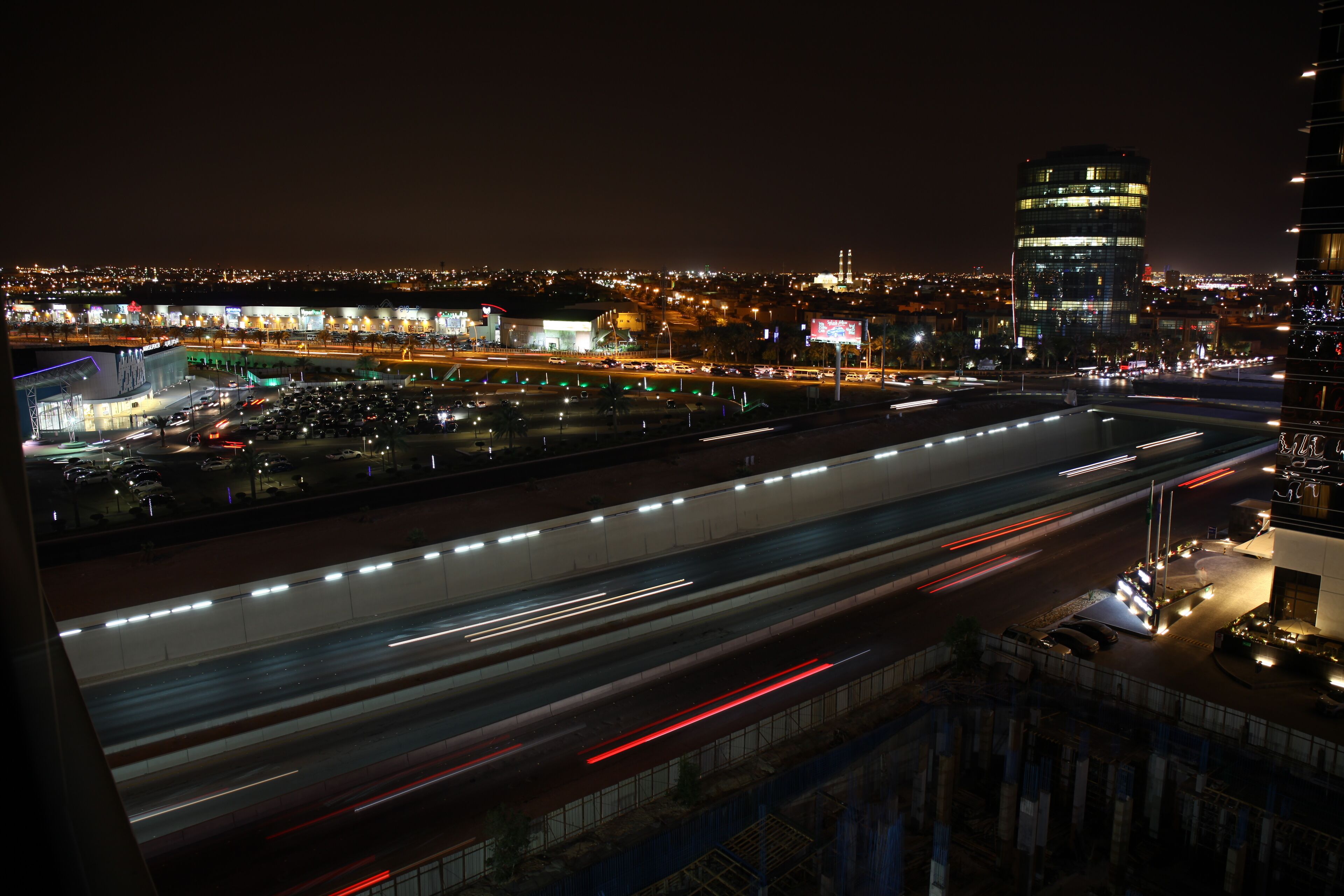 Een verlicht stadsbeeld 's nachts met gebouwen in de spotlights en een drukke snelweg.