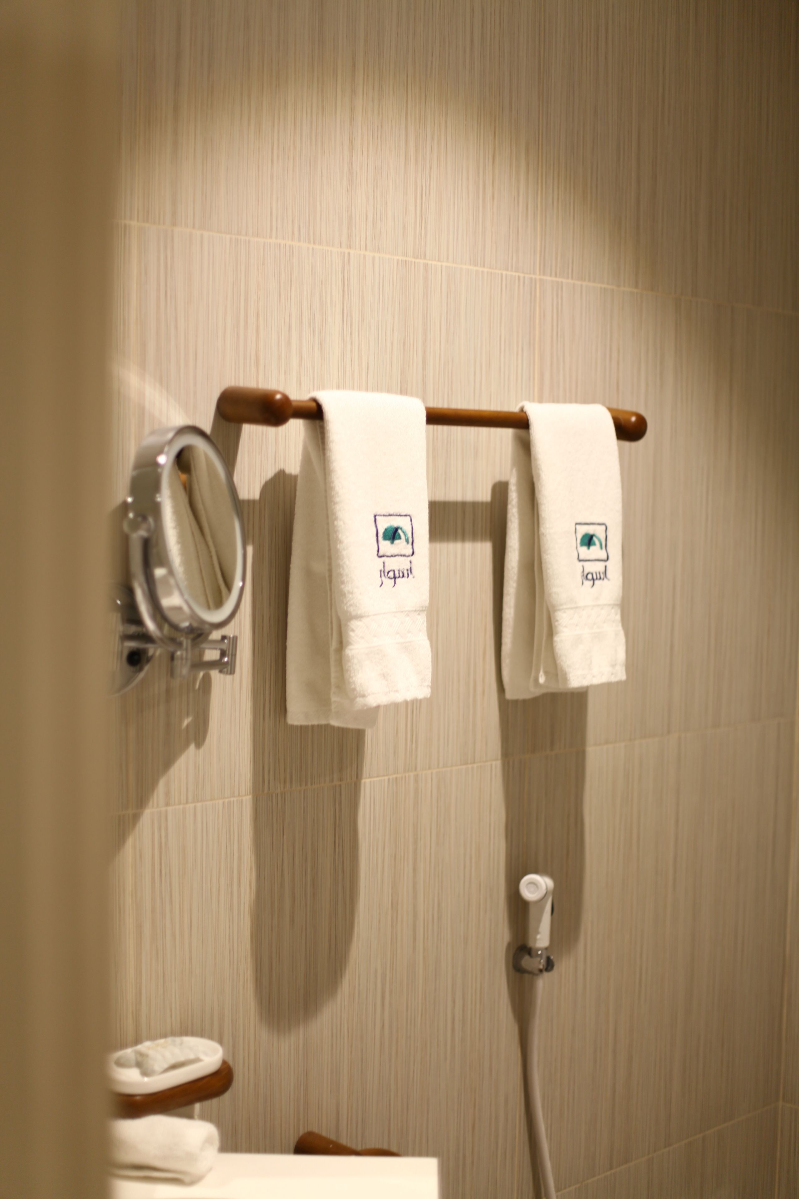 A bathroom with two white towels hanging on a wooden rack, a mirror, and a toilet.