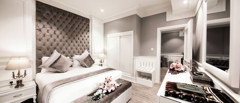 Un dormitorio moderno con un cabecero capitonado, una cama grande, mesitas de noche, un banco y un espejo grande.