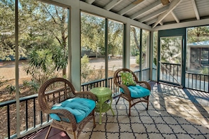 A covered porch with wicker chairs and a small table, overlooking a landscaped area with trees and a pathway. - Magnolia Cottages 163 Patina 3 Bedroom Holiday Home By Coastal Dreamin (Panama City Beach)