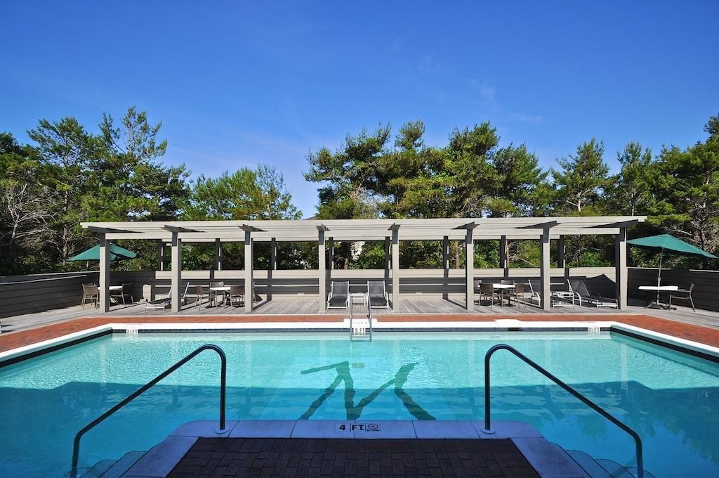 A swimming pool with a wooden deck and lounge chairs, surrounded by trees.