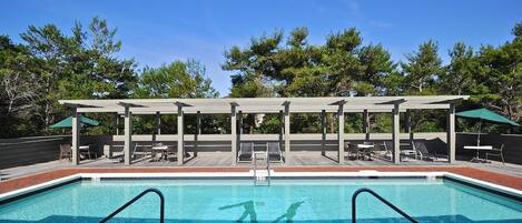 A swimming pool with a wooden deck and lounge chairs, surrounded by trees.